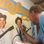 Brian Bain painting Foggy Mountain Breakdown, his portrait mural of Flatt & Scruggs at The Bluegrass Island Store in Manteo, NC