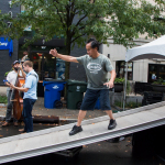 Soundman has fun and saves time going down from stage with his slide move. (Big Fat Gap warming up in background) at Wide Open Bluegrass 2016 - photo © Tara Linhardt