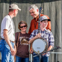 Riley Gilbreath with his parents as Steve Huber presents him with a new Huber Workhorse banjo - photo by Nathaniel Dalzell