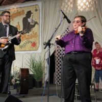 Katy Daley peeks out at Nathan Livers and Michael Cleveland at the 2018 Delaware Valley Bluegrass Festival - photo by Frank Baker