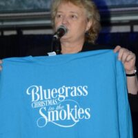 Host Lorraine Jordan shows off this year's T-shirt at 2018 Bluegrass Christmas in the Smokies - photo © Bill Warren