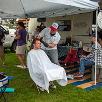 Caleb Duke Erickson giving Jeremy Stephens a trim as Corrina Rose Logston Stephens watches   85th Old Fiddlers Convention, Galax, VA - photo by Jeromie Stephens