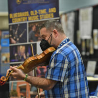 Dan Boner checks out a fiddle at the 2021 World of Bluegrass - photo © Bill Reaves