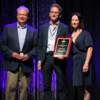 Dan Gabel of PegHead Nation accepts his Distinguished Achievement award from Sharon Gilchrist and Tim Stafford at the 2022 IBMA Industry Awards luncheon - photo © Frank Baker