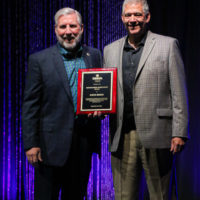 Steve Huber accepts his Distinguished Achievement award from Alan Tompkins at the 2022 IBMA Industry Awards luncheon - photo © Frank Baker