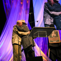 Jim Rooney embraces Peter Rowan during his Bluegrass Music Hall of Fame induction - photo © Frank Baker
