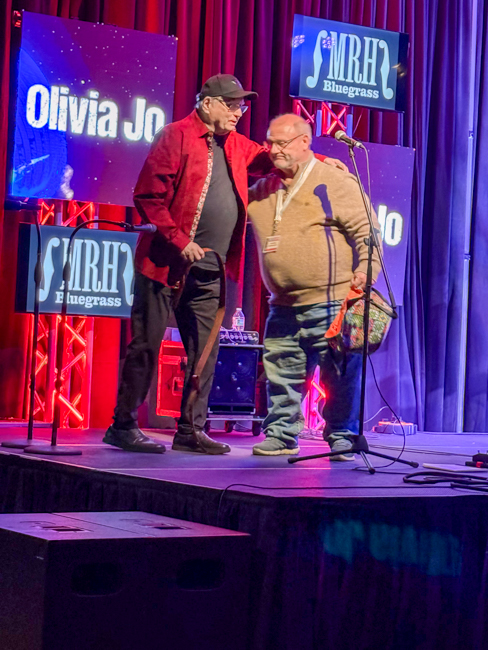 Mark Fisher presenting Milton Harkey with a guitar strap at Bluegrass First Class '26 - photo © Lisa Lambert Thompson