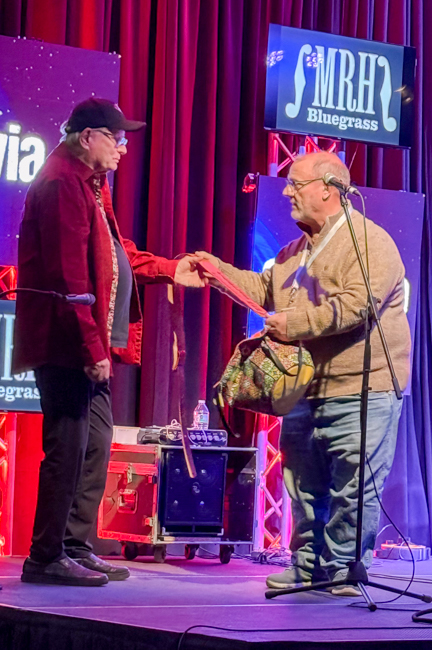 Mark Fisher presenting Milton Harkey with a guitar strap at Bluegrass First Class '26 - photo © Lisa Lambert Thompson