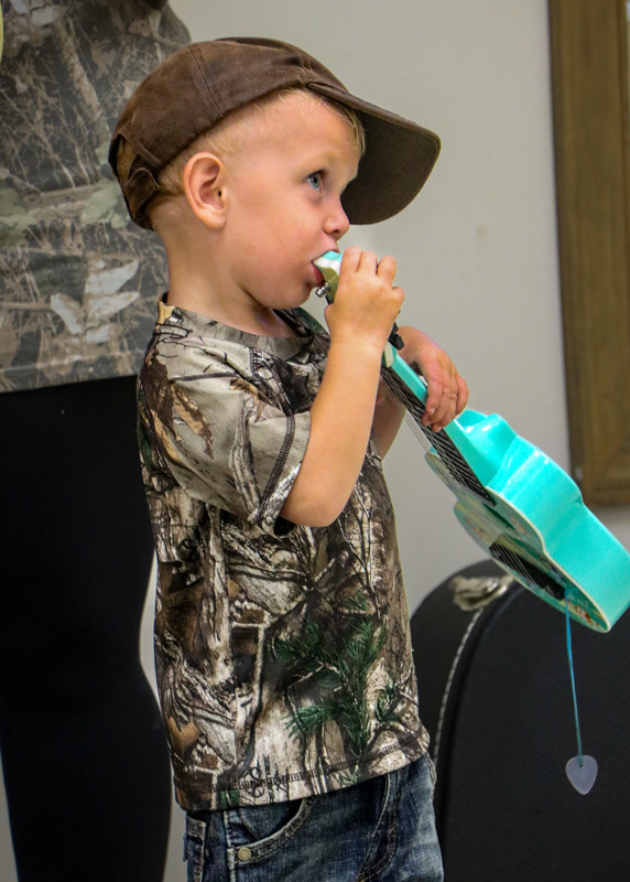 Boy chewing on guitar backstage at the 2026 Old Fiddlers’ Convention – photo © G. Nicholas Hancock